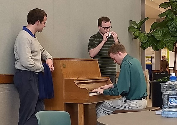 Jeremy, Tyler, and CJ gathered around a piano in the Wilkenson Student Center